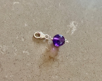 May include: A silver charm with a purple amethyst gemstone bead.