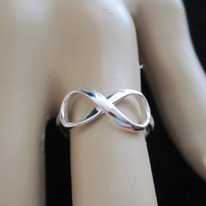 May include: A silver infinity ring with a smooth, polished finish. The ring is worn on a model's finger.