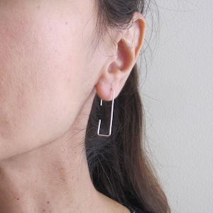 Puede incluir: Pendientes de aro rectangulares de plata. Los pendientes son simples y minimalistas en diseño.