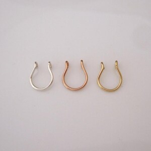May include: Three nose rings in different colours: silver, rose gold, and gold. The rings are all the same shape, a simple horseshoe.