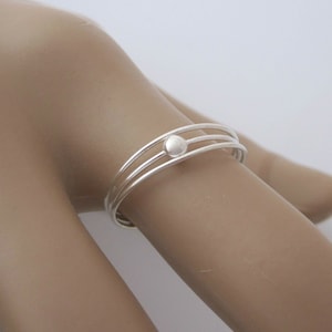 May include: A silver ring with three bands and a small round bead in the centre.