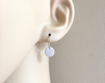 May include: A pair of silver hoop earrings with a small, round silver charm hanging from each hoop.