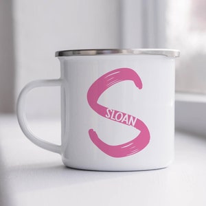 May include: White enamel mug with a pink 'S' and the name 'Sloan' written in white inside the 'S'.