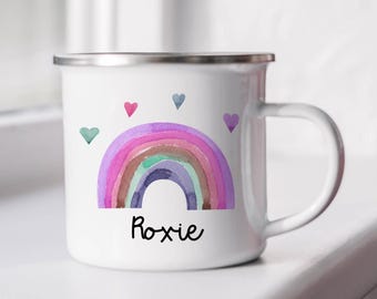 May include: A white enamel mug with a silver rim and a handle. The front features a watercolor-style rainbow in shades of purple, pink, and blue, surrounded by four small hearts in various colors. The name Roxie is printed in black script below.