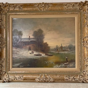Könnte beinhalten: Antikes Ölgemälde, das eine Winterlandschaft mit einem schneebedeckten Dorf, einem Fluss und einer Kirche in der Ferne zeigt. Das Gemälde ist in einem verzierten goldfarbenen Rahmen gerahmt, was seine Vintage-Ästhetik unterstreicht.
