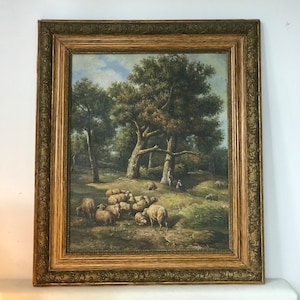 Könnte beinhalten: Ein gerahmtes Ölgemälde, das eine pastorale Szene mit einer Herde Schafe zeigt, die auf einer üppigen grünen Weide unter einem Blätterdach von Bäumen grasen. Das Gemälde ist in einer Waldlandschaft mit rustikalem Flair angesiedelt.