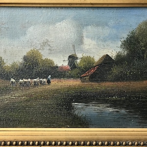 Op de afbeelding: Een schilderij van een landelijk landschap met een windmolen, een klein houten gebouw en een kudde schapen. De sc&egrave;ne is geschilderd in gedempte tinten bruin, groen en blauw, met een vleugje rood op het dak van het gebouw. Het schilderij is ingelijst in een gouden lijst.