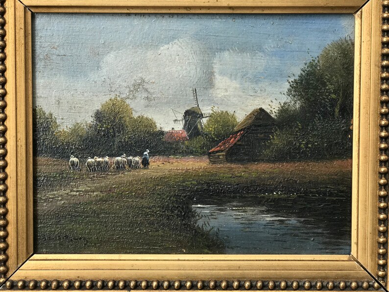 Op de afbeelding: Een schilderij van een landelijk landschap met een windmolen, een klein houten gebouw en een kudde schapen. De sc&egrave;ne is geschilderd in gedempte tinten bruin, groen en blauw, met een vleugje rood op het dak van het gebouw. Het schilderij is ingelijst in een gouden lijst.