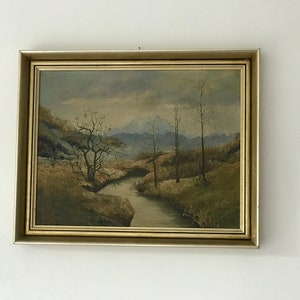 Könnte beinhalten: Ein gerahmtes Ölgemälde, das eine Landschaftsszene mit einem gewundenen Fluss darstellt, der durch ein Tal fließt. Das Gemälde zeigt eine gedämpfte Farbpalette mit Brauntönen, Grüntönen und Grautönen. Der Fluss ist von Bäumen und Hügeln umgeben, und der Himmel ist mit Wolken bedeckt.