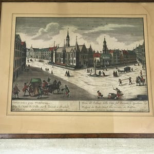 Puede incluir: Una impresión antigua que representa una plaza de la ciudad con edificios, una iglesia y personas caminando. La impresión está enmarcada en un marco de madera y tiene texto en inglés e italiano.