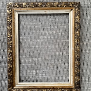 Könnte beinhalten: Rechteckiger antiker Bilderrahmen mit gold-cremefarbenem Finish. Der Rahmen hat verzierte florale Details an den Rändern. Der Rahmen ist leer und bereit, ein Foto oder Kunstwerk zu präsentieren.