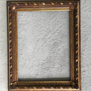 Könnte beinhalten: Verzierter rechteckiger Bilderrahmen mit gold-braunem Finish. Der Rahmen weist detaillierte Schnitzereien und einen dekorativen Rand auf. Der Innenraum ist leer, bereit für ein Foto oder Kunstwerk. Für die Wandmontage konzipiert.