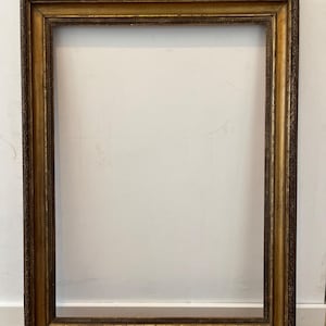 Könnte beinhalten: Ein rechteckiger, verzierter Bilderrahmen mit goldener Oberfläche. Der Rahmen hat detaillierte Schnitzereien und einen dunkelbraunen Innenrand. Der Rahmen ist leer und bereit, ein Foto oder Kunstwerk zu präsentieren. Der Rahmen ist ca. 61 cm hoch und 46 cm breit.