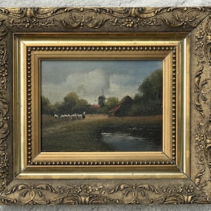 Op de afbeelding: Een ingelijst olieverfschilderij dat een landelijk landschap afbeeldt met een windmolen, een boerderij en een kudde schapen die grazen in een veld. Het schilderij is geplaatst tegen een bewolkte lucht en toont een klein beekje op de voorgrond.