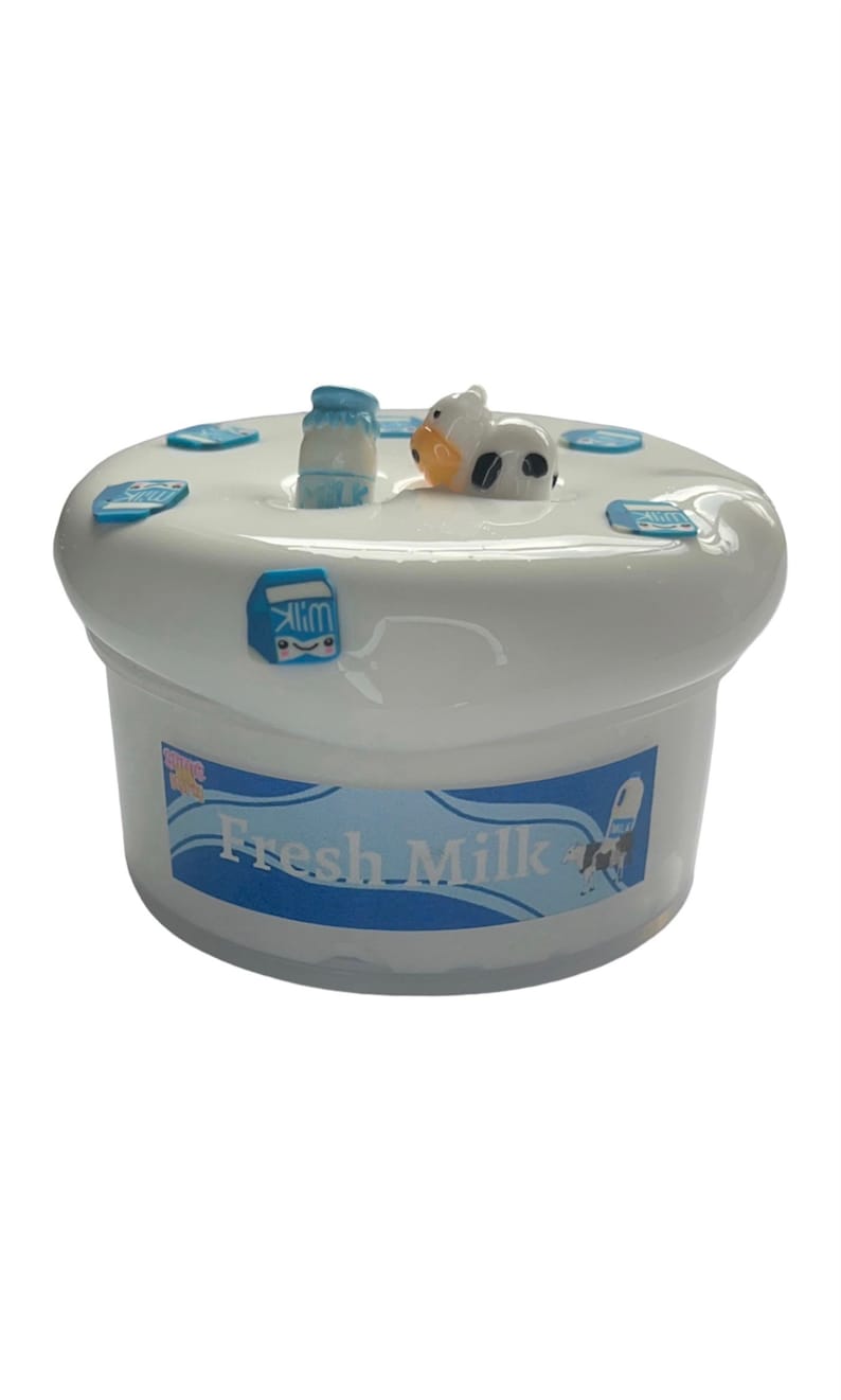 May include: White ceramic piggy bank shaped like a milk carton with a blue and white label that says "Fresh Milk". A small cow figurine is on top of the milk carton. There is a small milk bottle figurine on the top of the milk carton.