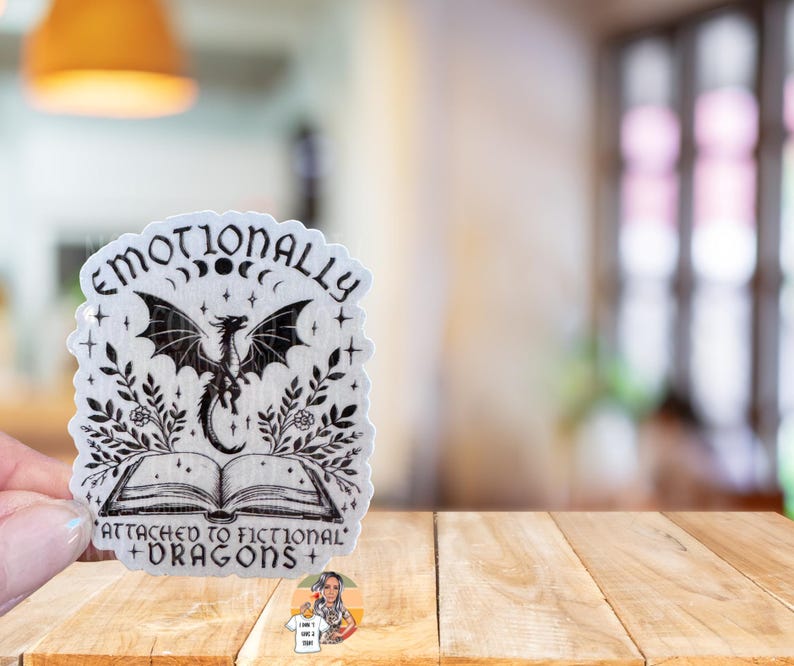 May include: A white sticker with black text and a black and white illustration of a dragon. The text reads "Emotionally Attached to Fictional Dragons".