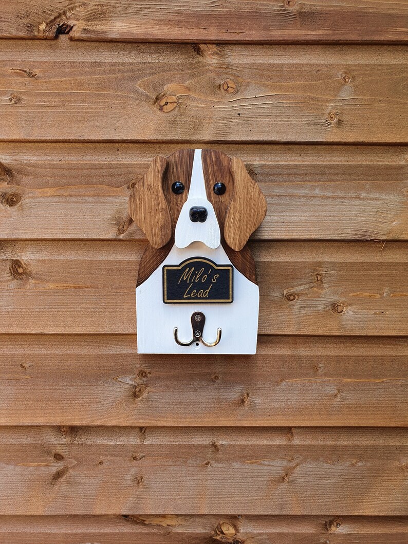 May include: Wooden dog-shaped key holder with two hooks. The dog is brown and white with black eyes and a black nose. The sign says "Milo's Lead".