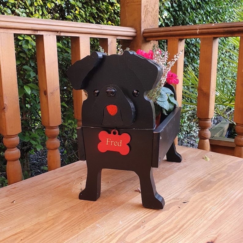 May include: Black wooden planter shaped like a pug dog with a red nose and a bone-shaped name tag that says "Fred".
