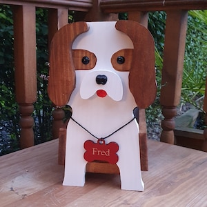 Op de afbeelding: Houten hondenplanter met bruine oren, wit lichaam en een rood botvormig label met de tekst "Fred".