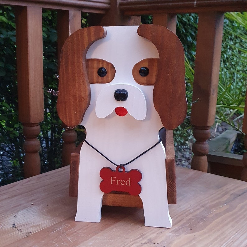 Op de afbeelding: Houten hondenplanter met bruine oren, wit lichaam en een rood botvormig label met de tekst "Fred".