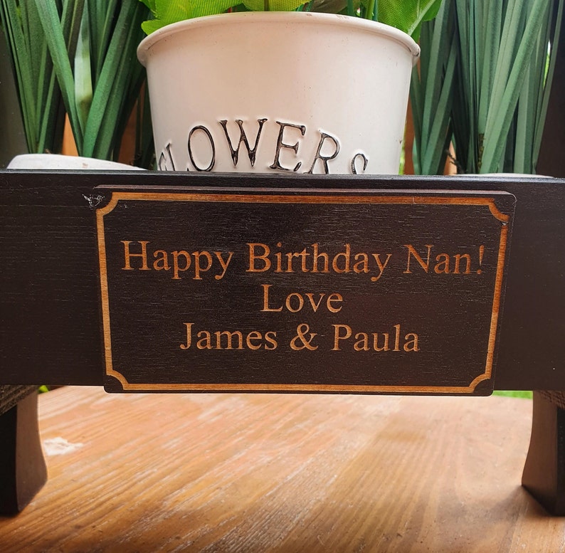 May include: A black wooden planter with a personalized plaque that reads "Happy Birthday Nan! Love James & Paula". The planter has a white pot with green plants inside.