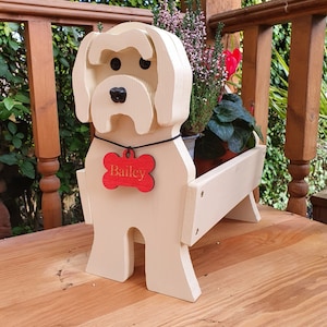 May include: A white wooden dog planter with a red bone-shaped tag that says "Bailey". The planter is holding a variety of green plants.