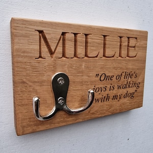 Könnte beinhalten: Haken aus Holz für die Hundeleine mit einem Doppelhaken und dem eingravierten Text "Millie" und "Eine der Freuden des Lebens ist es, mit meinem Hund spazieren zu gehen".