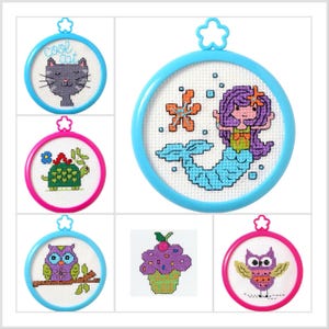 May include: A collection of cross-stitch kits featuring various designs. Included are a gray cat with the text "cool cat", a turtle, a mermaid, an owl on a branch, a cupcake, and an owl with outstretched wings. Each design is set in a round frame.