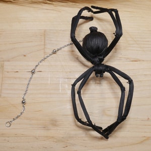 May include: Black spider made of woven straw with a silver chain attached to its back.