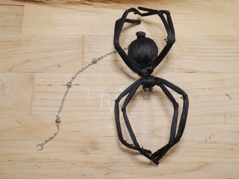 May include: Black spider made of woven straw with a silver chain attached to its back.