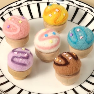 May include: A black and white striped plate with six small felt ice cream cones. The ice cream cones are in various colours, including pink, blue, yellow, purple, and brown. Each cone is decorated with colourful sprinkles.