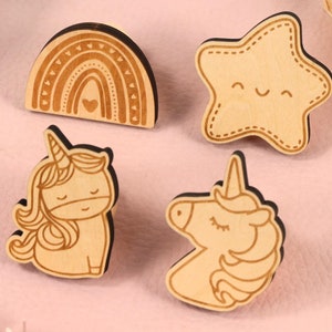 May include: Four wooden cutouts with a whimsical theme. A rainbow, a star with a smiling face, and two unicorns.
