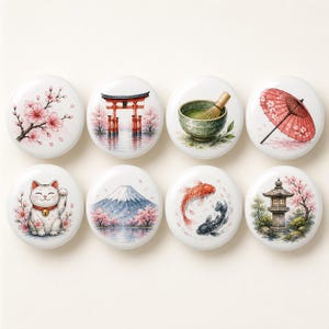 Könnte beinhalten: Ein Set aus acht runden, weißen Keramikknöpfen mit Aquarellillustrationen japanischer Motive, darunter Kirschblüten, ein Torii-Tor, eine Matchaschale mit Besen, ein roter Regenschirm, eine Winkekatze, der Berg Fuji, Koi-Karpfen und eine Steinlaterne.