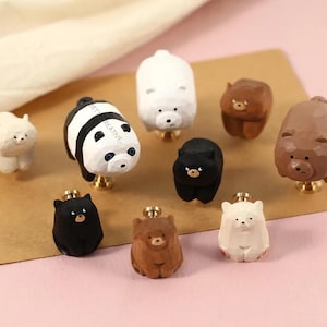 Könnte beinhalten: Eine Sammlung von schrankknöpfen in Bärenform in verschiedenen Farben, darunter Weiß, Schwarz und Braun. Ein Knopf hat ein Panda-Design. Die Knöpfe sind auf Messingbeschlägen montiert.