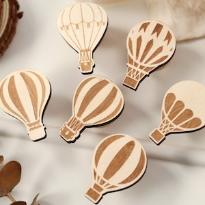 May include: Six wooden hot air balloon ornaments in various designs. The balloons are all light brown with darker brown details.
