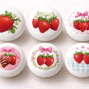 May include: A collection of six white ceramic knobs, each adorned with a vibrant strawberry design. The illustrations feature red strawberries with green leaves, some with floral or bow accents. The knobs are perfect for adding a touch of whimsy to furniture.