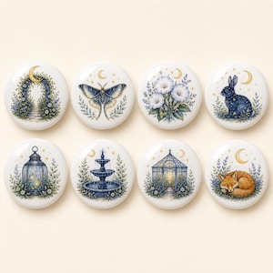 Könnte beinhalten: Ein Set aus acht runden, weißen Keramikknöpfen mit detaillierten Gartenmotiven, darunter ein Steinbogen, ein Nachtfalter, Blumen, ein Hase, eine Laterne, ein Brunnen, ein Pavillon und ein schlafender Fuchs, jeweils unter einem abgebildeten Halbmond.