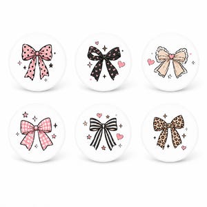 May include: Six white decorative buttons with bow designs. The bows feature various patterns, including polka dots, hearts, gingham, and leopard print. Each button has a different color scheme, such as pink, black, and tan, with star and heart accents.