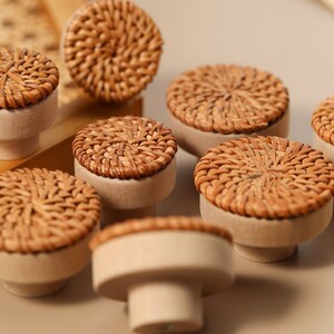 May include: Eight brown wicker drawer knobs with a natural wood base. The knobs have a woven pattern and are arranged on a light brown surface.