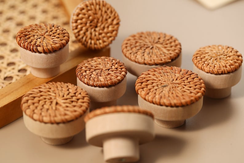 May include: Eight brown wicker drawer knobs with a natural wood base. The knobs have a woven pattern and are arranged on a light brown surface.