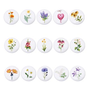 Puede incluir: Conjunto de 16 azulejos de cerámica redondos con diferentes diseños florales. Cada azulejo muestra una flor diferente, incluyendo campanillas, lirios, margaritas y flores silvestres, pintadas en colores vibrantes sobre un fondo blanco.