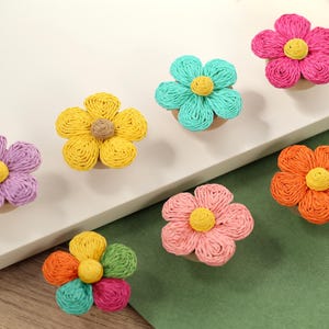 Könnte beinhalten: Sechs bunte Papierblumen mit gelben Zentren. Die Blumen sind aus gedrehtem Papier gefertigt und in einer Reihe auf einer weißen Oberfläche angeordnet.