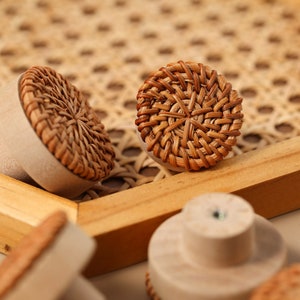 May include: Close-up of five round, woven rattan knobs with a natural brown color. The knobs are on a wooden surface with a woven pattern.