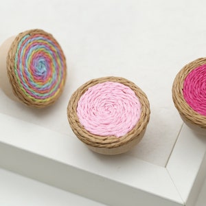 May include: Five colorful round decorative knobs with a brown paper base and a spiral design in the center. The colors are rainbow, pink, red, teal, and white.