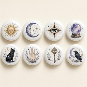 Könnte beinhalten: Ein Set aus acht runden weißen Knöpfen mit Illustrationen von Sonne, Mondsichel, Auge, Kristallkugel, schwarzer Katze, Handlesehand, verziertem Schlüssel und Rabe, jeweils umgeben von kleinen Sternen und botanischen Elementen.