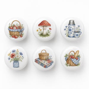 Peut inclure: Un ensemble de six boutons en céramique blanche ronde, chacun présentant une illustration distincte : un panier de fraises, un champignon rouge, un thermos et une tasse à motifs floraux bleus, un bouquet de fleurs sauvages dans un bocal à carreaux bleus, un panier de pique-nique sur une couverture, et un panier avec du pain et des fraises.