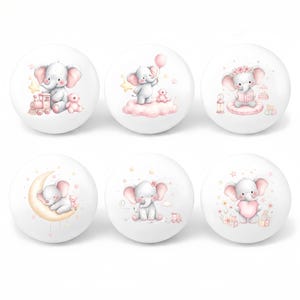 May include: Six white decorative knobs with charming elephant illustrations. Each knob features a different design, including an elephant with a train, on a cloud, reading a book, on a moon, with flowers, and holding a heart. The elephants are in soft pink and grey tones.