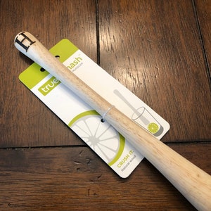 May include: A wooden muddler with a textured end and the letter "H" carved into the top. The muddler is on a white and green package that says "true mash muddler" and "crush it. natural wood".