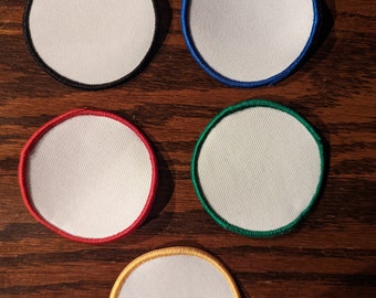 May include: Five blank, circular patches with white centers and colored borders: black, blue, red, green, and gold. The patches are arranged on a dark wood surface, offering a clean and organized presentation.