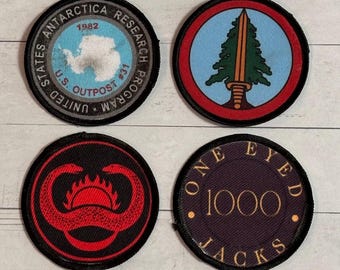 Puede incluir: Cuatro parches redondos bordados. Uno presenta un mapa de la Antártida con el texto "U.S. Outpost #31" y "United States Antarctica Research Program 1982". Otros parches tienen un árbol y una espada, un diseño rojo sobre negro y "One Eyed 1000 Jacks".